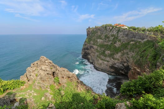 Overview panorama ocean shore, cliff. Overwhelmed scene the flower and green-capped vertical cliff over the Indian ocean. South of Bali island, Pura Luhur Uluwatu Temple. Indonesia.