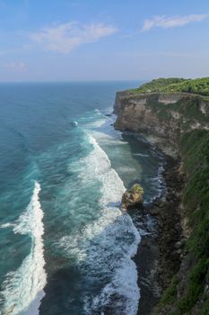View of Uluwatu cliff with pavilion and blue sea in Bali, Indonesia. Beautiful scenery of Pura Luhur Uluwatu Temple with colorful flowers foreground during day. Scenic coastal landscape of high cliff.