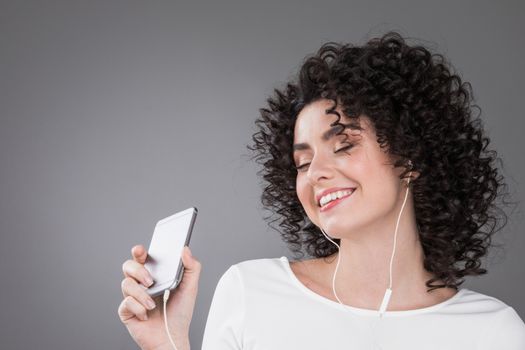 Woman in white dancing with earphones headphones listening to music on phone, gray background