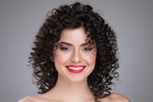 Beauty young woman portrait on gray background. Girl with black curly hair. Hairstyle. Haircut