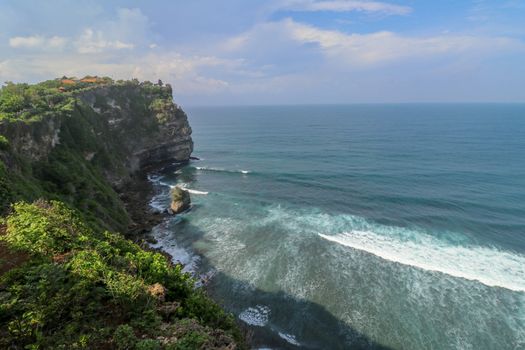 Overview panorama ocean shore, cliff. Overwhelmed scene the flower and green-capped vertical cliff over the Indian ocean. South of Bali island, Pura Luhur Uluwatu Temple. Indonesia.