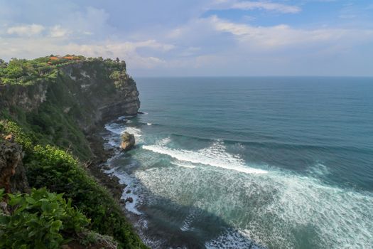 Overview panorama ocean shore, cliff. Overwhelmed scene the flower and green-capped vertical cliff over the Indian ocean. South of Bali island, Pura Luhur Uluwatu Temple. Indonesia.