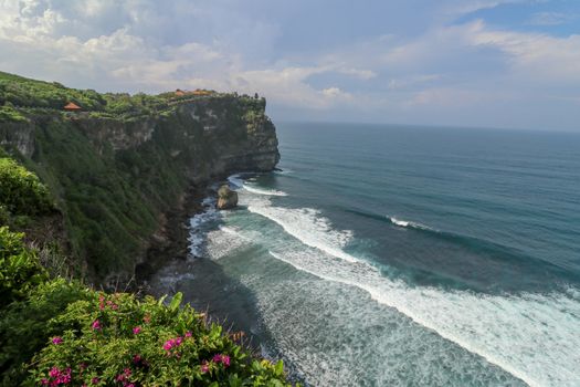 Overview panorama ocean shore, cliff. Overwhelmed scene the flower and green-capped vertical cliff over the Indian ocean. South of Bali island, Pura Luhur Uluwatu Temple. Indonesia.
