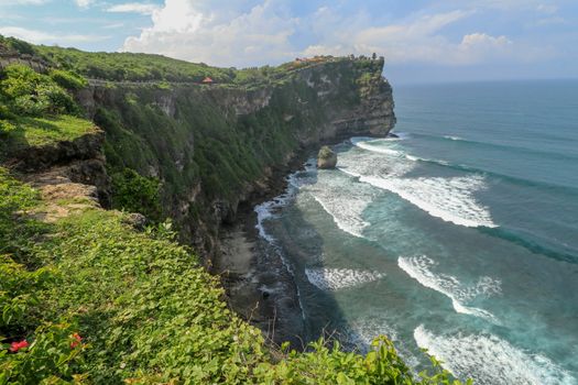 Overview panorama ocean shore, cliff. Overwhelmed scene the flower and green-capped vertical cliff over the Indian ocean. South of Bali island, Pura Luhur Uluwatu Temple. Indonesia.
