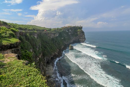 Overview panorama ocean shore, cliff. Overwhelmed scene the flower and green-capped vertical cliff over the Indian ocean. South of Bali island, Pura Luhur Uluwatu Temple. Indonesia.