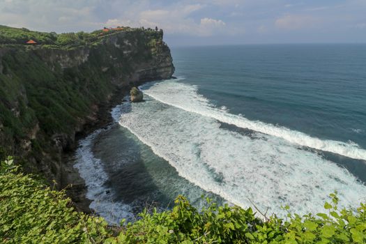 Overview panorama ocean shore, cliff. Overwhelmed scene the flower and green-capped vertical cliff over the Indian ocean. South of Bali island, Pura Luhur Uluwatu Temple. Indonesia.