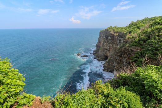 Overview panorama ocean shore, cliff. Overwhelmed scene the flower and green-capped vertical cliff over the Indian ocean. South of Bali island, Pura Luhur Uluwatu Temple. Indonesia.