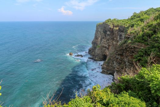 Overview panorama ocean shore, cliff. Overwhelmed scene the flower and green-capped vertical cliff over the Indian ocean. South of Bali island, Pura Luhur Uluwatu Temple. Indonesia.