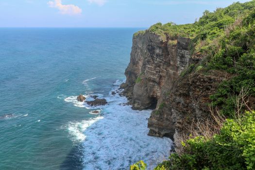 Overview panorama ocean shore, cliff. Overwhelmed scene the flower and green-capped vertical cliff over the Indian ocean. South of Bali island, Pura Luhur Uluwatu Temple. Indonesia.