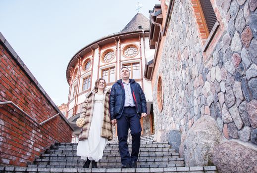 couple of newlyweds are walking near the old castle on cold early spring day