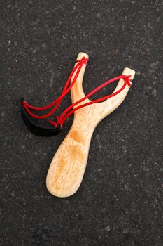 Simple slingshot isolated, wooden handle with two red rubber bands attached to a black leather strip used to put things to be shot on black background. Primitive but effective weapon.