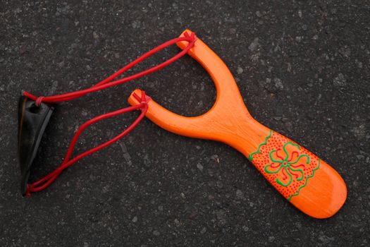 Handmade orange slingshot catapult. Y-shaped wooden stick with elastic tied between two top parts. Slingshot or Catapult is a device for shooting small stones.