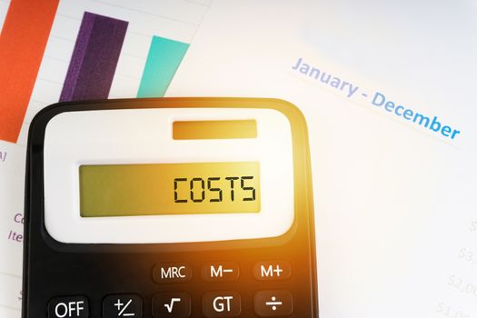 A calculator with the word COSTS on the display. Selective focus and crop fragment