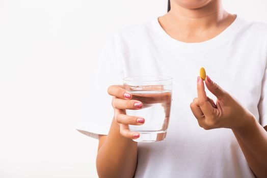 Closeup young Asian woman hold fish oil vitamin drugs in hand ready take medicines with a glass of water, studio shot isolated on white background, Healthcare and medical pharmacy concept