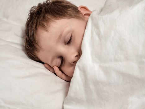 Sleeping young boy. Four-year-old boy sleeping in white bed. Close up, copy space