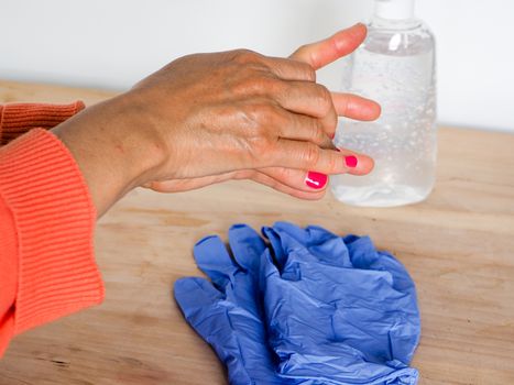 close up of  woman hands while cleaning and sanitizing  herself  with anti virus bacterial gel against covid-19 , fall dress, orange color over a wood table, earth tones.