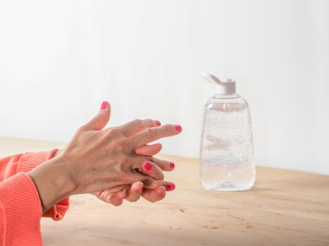 close up of  woman hands while cleaning and sanitizing  herself  with anti virus bacterial gel against covid-19 , fall dress, orange color over a wood table, earth tones.