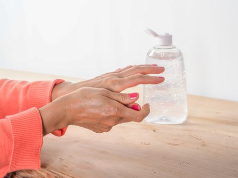 close up of  woman hands while cleaning and sanitizing  herself  with anti virus bacterial gel against covid-19 , fall dress, orange color over a wood table, earth tones.