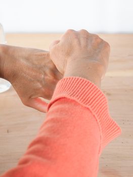 close up of  woman hands while cleaning and sanitizing  herself  with anti virus bacterial gel against covid-19 , fall dress, orange color over a wood table, earth tones.