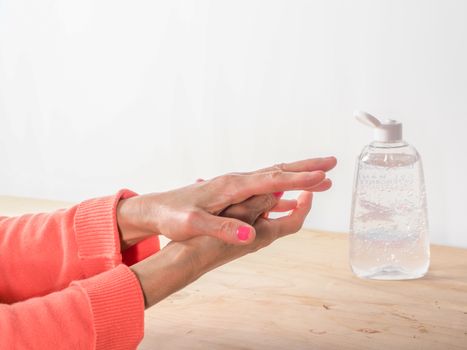 close up of  woman hands while cleaning and sanitizing  herself  with anti virus bacterial gel against covid-19 , fall dress, orange color over a wood table, earth tones.