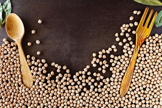 Composition of natural chickpeas with kitchen utensils, spoon and wooden fork on rustic textured bottom. View from above with space to write