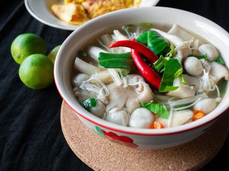 Food Thai name is Mushroom Tom Yum,Ingredients mushroom chilli lemon lemon grass Kaffir lime leaves Galangal and Coriander,saw blade,Black fabric background,Omelette, side dish