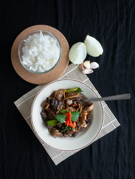 Fried Pork Entrails name is Phad cha Thai food,The ingredients Pork Filling Chilli Pepper Krachai Garlic Onion and Kaffir lime leaves,Rice in a cup,Background color Black