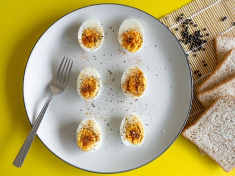 Boiled egg topped with Cayenne pepper Pepper and Salt on a white dish,Egg colors white and yellow,Eat with bread