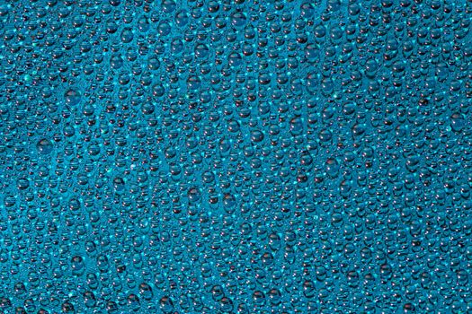 water drops on aurora green pearl glass of modern phone back cover, close-up with selective focus and blur.