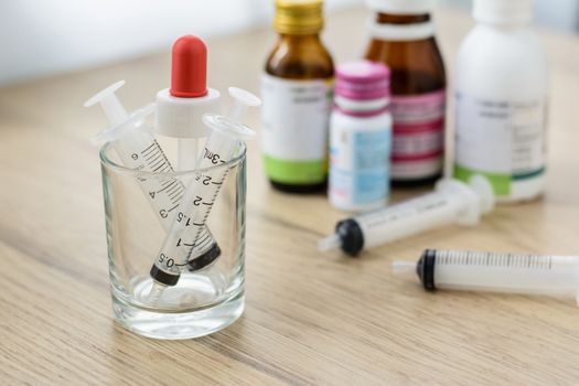 Empty syringes barrel in the small glass on the wooden table with blured medicine bottle background.