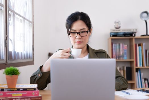 Modern young Asian woman working from home and drinking a coffee.