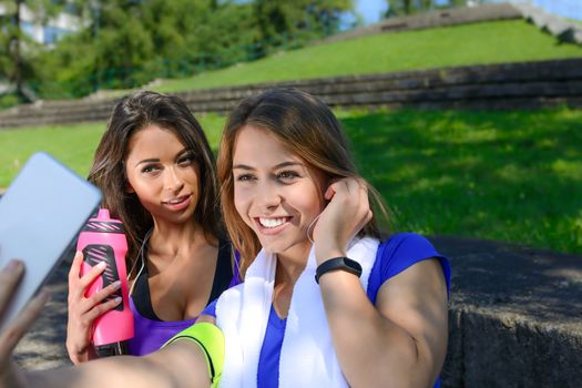 Millennial generation lifestyle concept - two sports girls taking a selfie and smiling after outdoors training on a sunny day.