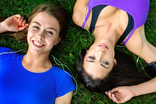 Top view of two beautiful and young girls resting on the grass after outdoor workout on a sunny day