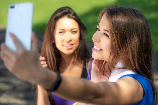 Millennials lifestyle concept - two sports girls taking a selfie and smiling after outdoors training on a sunny day.