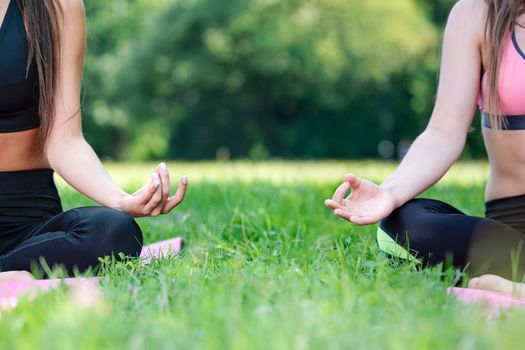 Two women doing yoga meditation in a lotus pose outdoors in a park on a sunny day in close-up (copy space)