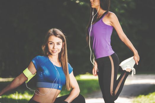Two young and fit girls stretching before jogging in the park on a sunny morning (vintage effect)