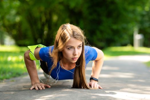 Fitness and healthy lifestyle concept - cute girl doing push-up exercise on the park in a sunny morning in close-up