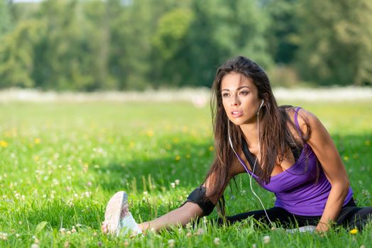 Portrait of a beautiful young girl stretching before jogging on the grass in the park on a sunny morning (copy space)