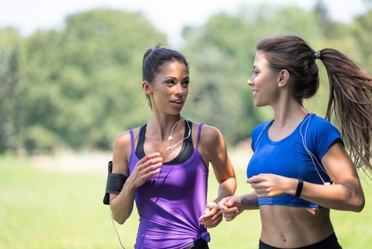 Two beautiful and attractive fitness girls are jogging in the park on a sunny morning