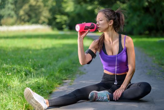 Cute girl resting and drinking after hard workout in the park on a sunny morning.