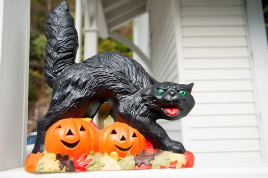 Black cat snarling while walking over jack o lantern face cutouts on halloween themed statue