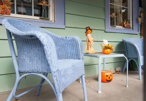 quaint front porch on street with blue wicker chairs and halloween decorations.