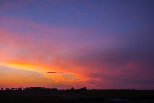 Natural Sunset Sunrise Over Field Or Meadow. Bright Dramatic Sky And Dark Ground. Countryside Landscape Under Scenic Colorful Sky At Sunset Dawn Sunrise. Sun Over Skyline, Horizon. Warm Colours.