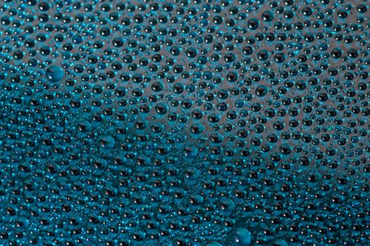 water drops on aurora green pearl glass of modern phone back cover, close-up with selective focus and blur.