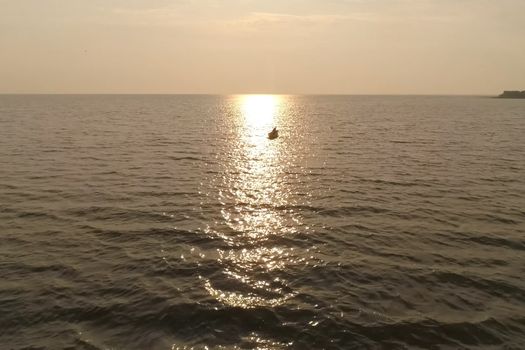 A fisherman in a boat in the sea against the sunset.