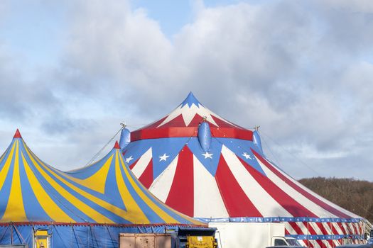 Red and white circus tent topped with bleu starred cover against a sunny blue sky with clouds