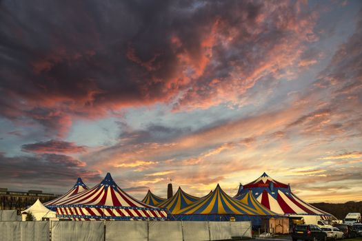 Red and white circus tents topped with bleu starred cover against a sunny blue sky with clouds