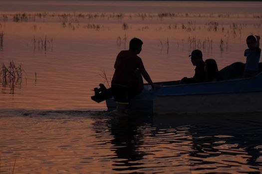 Silhouettes of fishermen on the river near the boat. Pushing the boat.