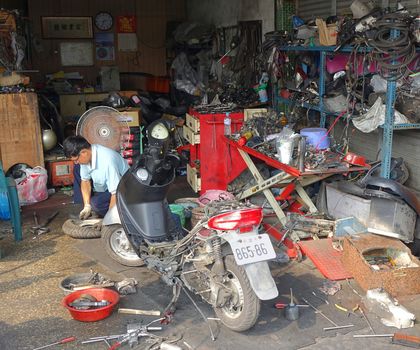 KAOHSIUNG, TAIWAN -- OCTOBER 17, 2015: A man fixes a tire in a local scooter repair shop.
