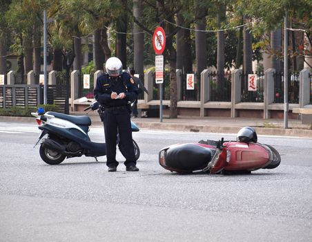 KAOHSIUNG, TAIWAN -- FEBRUARY 8, 2014: A policeman records the details of a traffic accident involving a motor scooter.